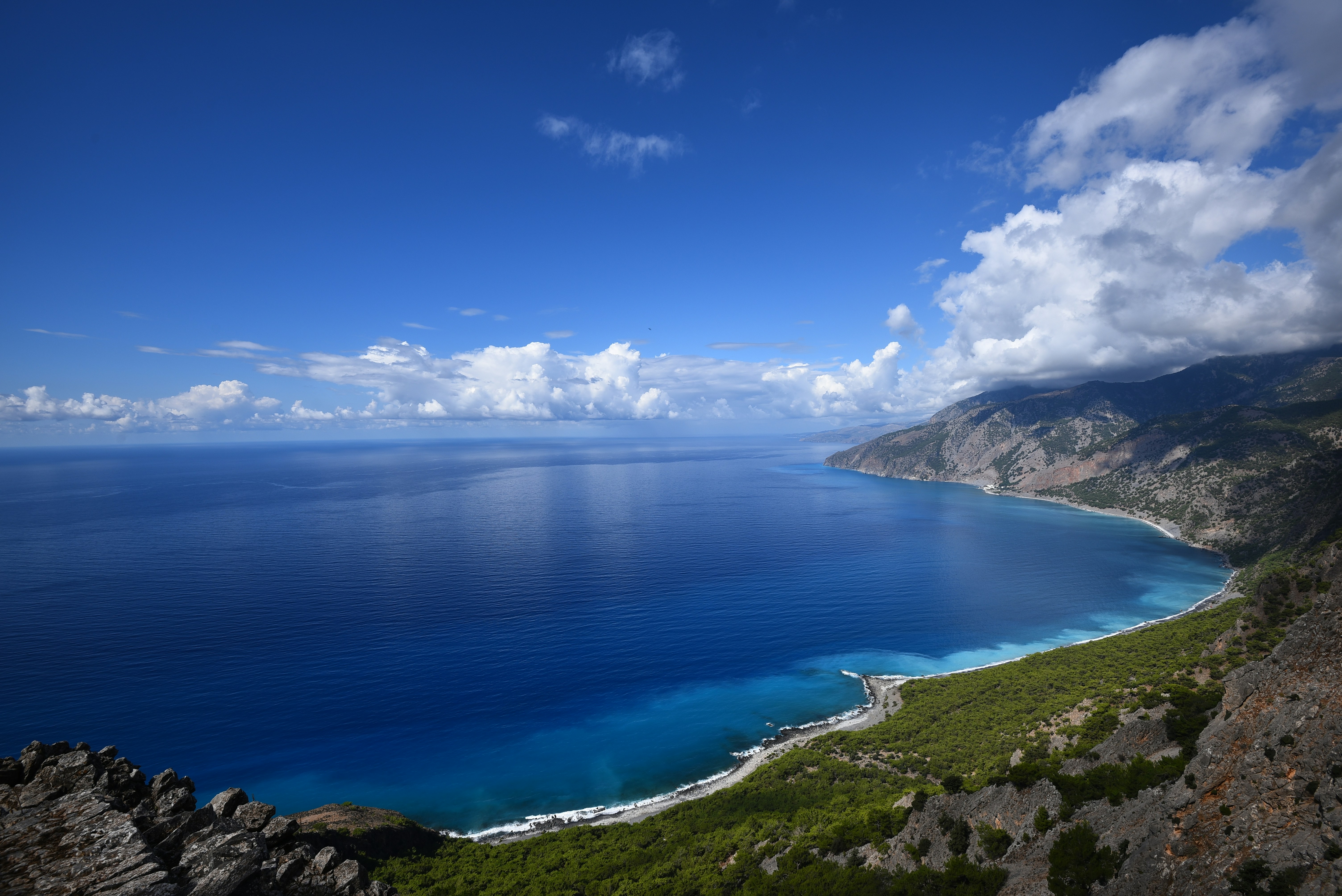 A scenic view of the Greek coastline with fish farms floating on the deep blue sea.