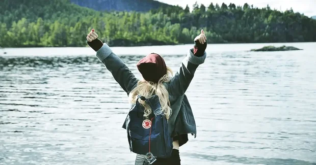 girl in backpack celebrating by lake
